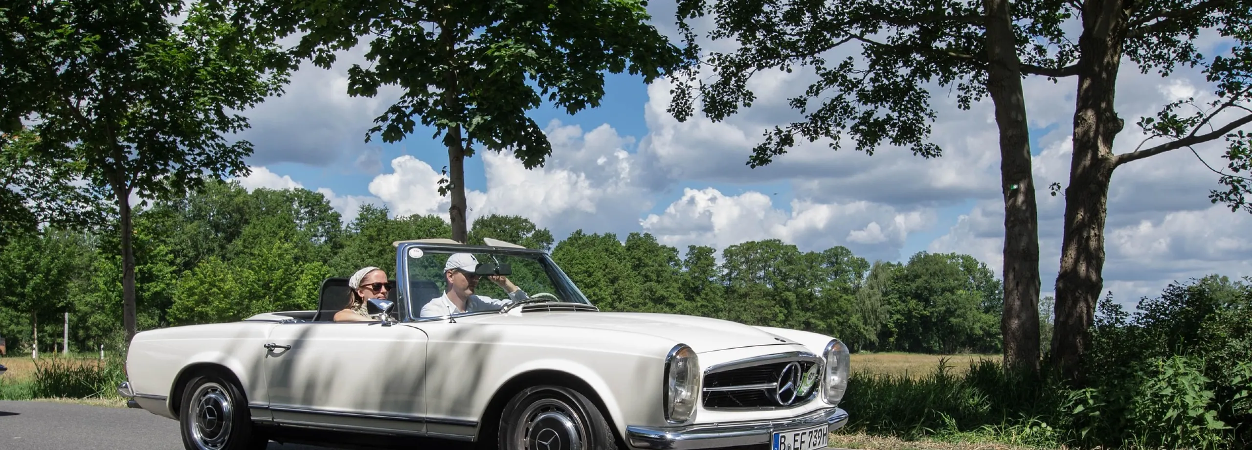Äldre vit mercedes som kör på en sommarväg